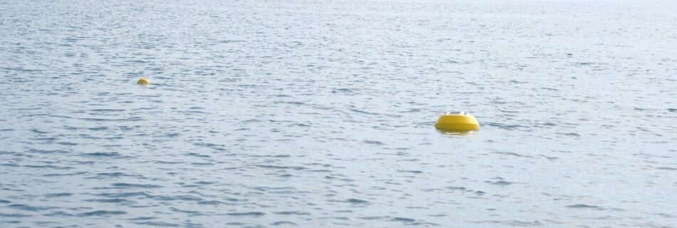 An Obscape monitoring buoy floating in the open ocean, with a cargo ship on the horizon