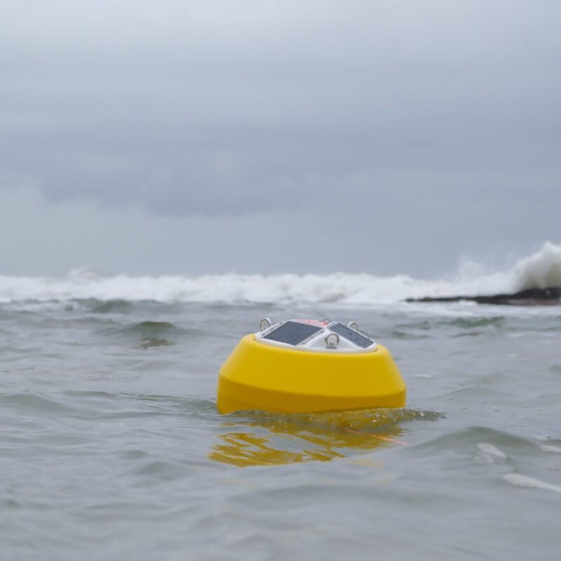 An Obscape OBS-Buoy 7 Watt floating at sea with surf breaking on rocks behind