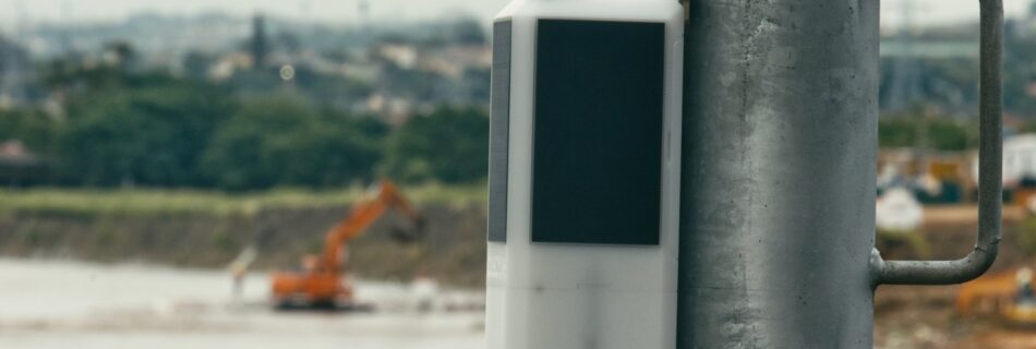 An Obscape water-level monitoring station mounted on a pole above a river, with earthmoving equipment in the background
